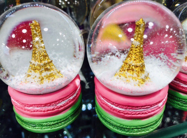 Boule de neige avec la Tour Eiffel dorée et deux macarons colorés, souvenir de Paris.